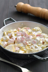 tortellini ripieni con panna e prosciutto ,in tegame di metallo su sfondo grigio