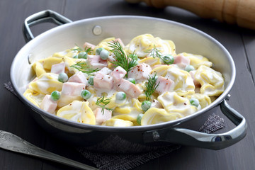 tortellini ripieni con panna ,prosciutto e piselli,in tegame di metallo su sfondo grigio