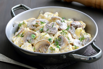 tortellini ripieni con panna ,funghi e piselli,in tegame di metallo su sfondo grigio
