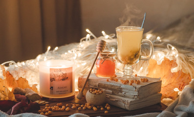 Tea with sea-buckthorn berries and ginger on old books, honey, candle and autumn leaves. The atmosphere of comfort at home. Cozy