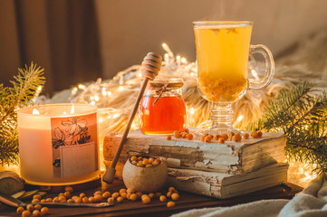 Tea with sea-buckthorn berries and ginger on old books, honey, candle and conifer branches. The...