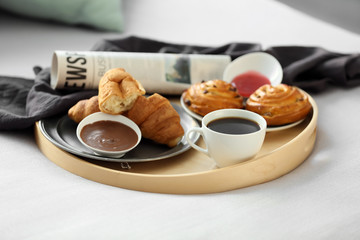 Tray with delicious breakfast and newspaper on bed