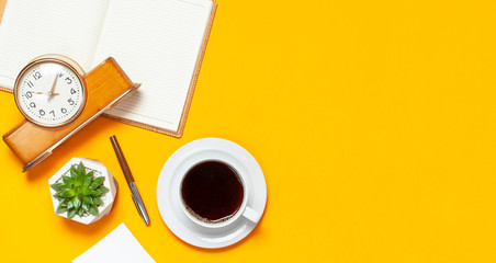 Cup of coffee, open notebook with blank pages, retro alarm clock, pen, cactuses succulents on bright yellow minimalistic background top view Flat Lay with copy space. Still life, concept of business