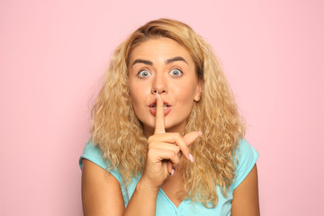 Portrait of beautiful young woman showing silence gesture on color background