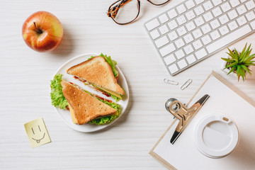 top view of workplace with sandwich, paper coffee cup, apple and symbol of smile at table in office