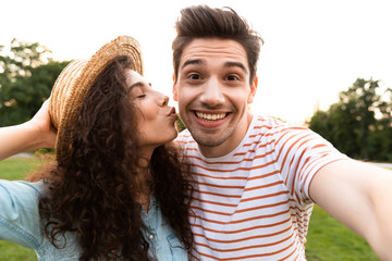 Fototapeta premium Image of funny people man and woman 20s walking in green park, and taking selfie on cell phone