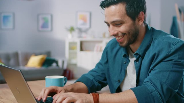 Portrait of Handsome Hispanic Man Working on a Laptop while Sitting at His Desk in the Cozy Living Room. Happy Man Uses Computer at Home.