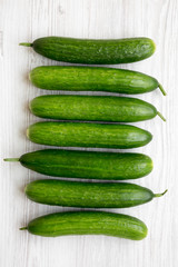 Raw organic green cucumbers on white wooden background, overhead view. Flat lay, from above, top view.