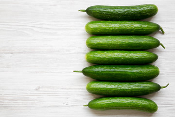 Raw organic green cucumbers on white wooden table, overhead view. Flat lay, from above, top view. Copy space.