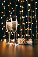 glasses of champagne and present on garland light background, christmas concept © LIGHTFIELD STUDIOS