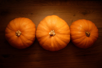 Three orange pumpkins on a wooden background.