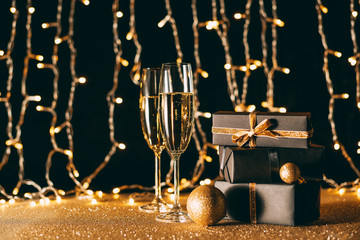 christmas presents and glasses of champagne on garland light background