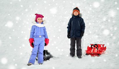 childhood, sledging and season concept - happy little kids with sleds in winter