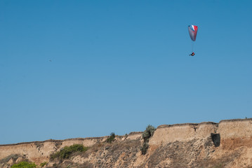 Paraglider hovering over the cliff and the landscape of the sea, soaring on the rising air, extreme...