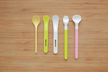 Different type of plastic spoons for babies on wood board background.