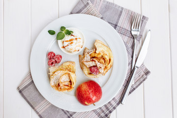 Crepes, thin pancakes with fresh strawberry and ice-cream, on white plate. Wooden background. Top view