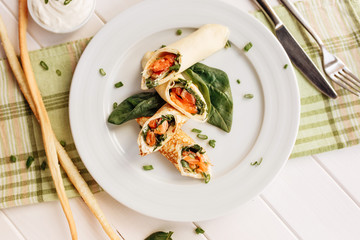 Rolls of thin pancakes with smoked salmon, horseradish cream cheese and spinach leaves. Side view with copy space