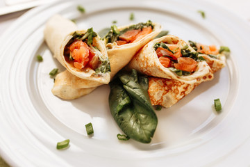 Rolls of thin pancakes with smoked salmon, horseradish cream cheese and spinach leaves. Side view with copy space