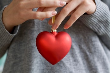 Frauenhände halten eine Weihnachtskugel in Form eines rot leuchtenden Herz.