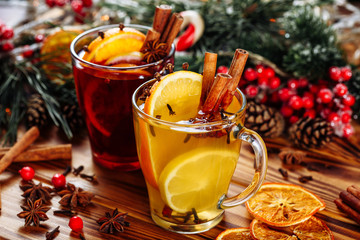 Two glasses of hot mulled wine with oranges and spices on wooden background. Close-up side view