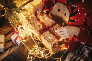 girl hands opening Christmas gift box on at golden beautiful christmas tree with lights in festive room. winter holiday atmospheric moments. seasons greetings. Merry Christmas