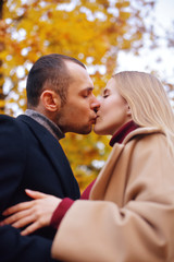 Fototapeta premium Girl and man or lovers on date hug. Couple in love in park . Autumn. Man and woman smile on autumn fallen leaves in a park, enjoying a beautiful autumn day. Young couple in the autumn. Kiss