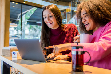 Multiracial girls smiling using a laptop drinking coffee at the bar