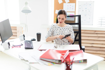 A young girl sitting in the office at the table, said on the calculator and working with documents.