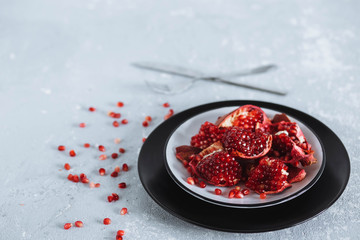 Close-up food photo. Ripe red pomegranate and pieces on a plate on a gray table