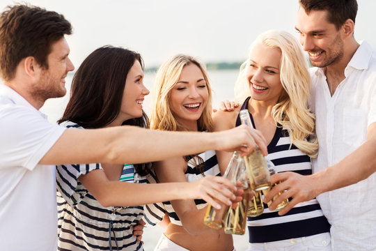 friendship, summer holidays and people concept - group of happy friends in striped clothes drinking non alcoholic beer on beach