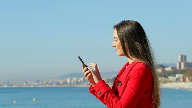 Side view portrait of an excited woman using a smart phone on the beach in winter. Slow motion