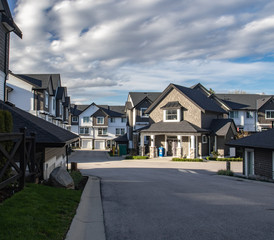 Row of new residential townhouses on a street. Family townhouses with concrete driveways and asphalt road in front.