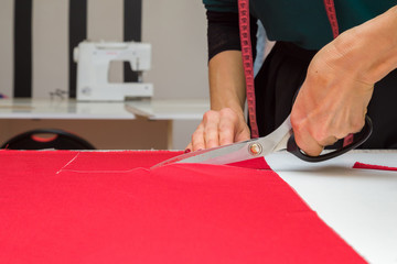 Woman's hands cutting bright red fabric on sketch lines with scissors. Preparing details of material for new, modern, classic dress, blouse, trousers or other clothes. Handmade work. Feminine hobby.