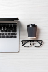 top view of arranged laptop, eyeglasses and paper coffee cup at table in office, minimalistic concept