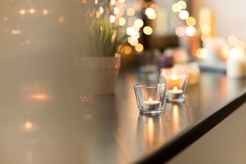 hygge, decoration and christmas concept - candles burning in lanterns and festive garland on window...