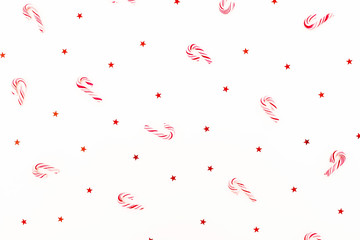 Christmas pattern made of candy cane and red shiny confetti on white background. Flat lay, top view.
