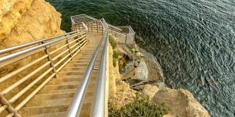 Sunlit stairs on a cliff going down the calm ocean