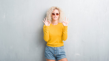 Young blonde woman with curly hair over grunge grey background relax and smiling with eyes closed doing meditation gesture with fingers. Yoga concept.