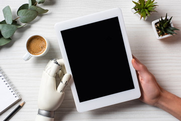 partial view of businessman with prosthesis arm using digital tablet with blank screen at table with coffee cup in office