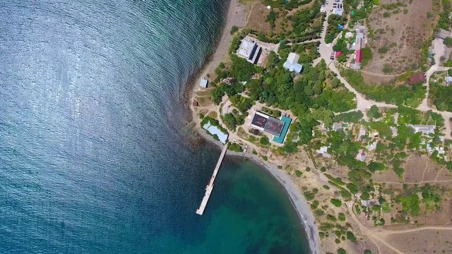Top view aerial footage motion pier for yachts and sailboats, glare on water, beach of Karadak vulcan. Flying perfect Crimea beach background dock and boat, bird's eye view travel beautiful sea.