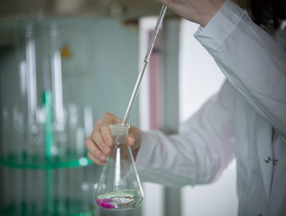 Chemical laboratory. Young woman holding a flask, dripping something using pipette. The liquid...