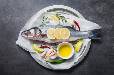 Fresh fish sea bass and ingredients for cooking. Raw fish sea bass with spices and herbs on black slate table copy space.