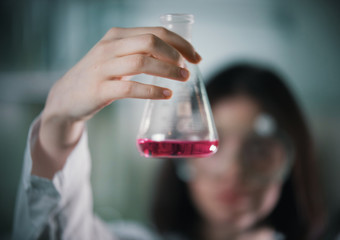 Chemical laboratory. Young woman holding a flask with liquid in it. Flask in focus