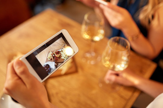 people, technology and lifestyle concept - hand of woman picturing food by smartphone and drinking wine at bar or restaurant
