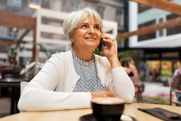 technology, old age and people concept - happy senior woman with coffee calling on smartphone at street cafe