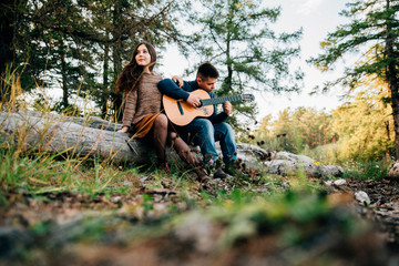 young man playing guitar while woman smiling on meadow