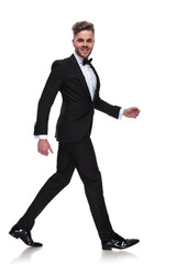 laughing young man in tuxedo and bow tie is walking