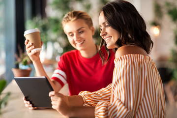 technology and people concept - female friends with tablet pc computer and coffee at cafe