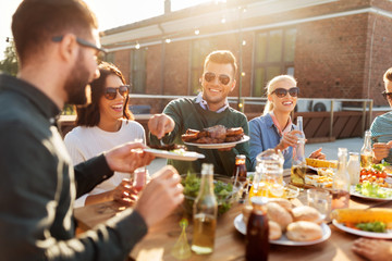 leisure and people concept - happy friends eating and drinking at barbecue party on rooftop in summer
