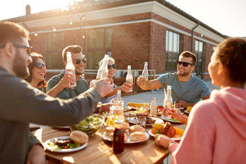 leisure and people concept - happy friends toasting drinks dinner or barbecue party on rooftop in...